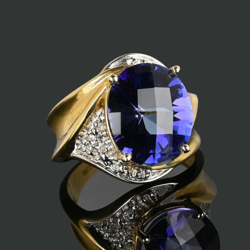 Flashy and bodacious vintage ring with a checkerboard tanzanite gemstone with diamond cluster accents on the side. Set in 10K yellow gold, the vibrant bluish-purple 6-carat tanzanite is set in a raised gallery, with the diamonds set in a swirl pattern of white gold around the gemstone. A very unique fluted band completes the piece. A wonderful statement ring with the birthstone of December. A fabulous statement ring!

https://boylerpf.com/products/vintage-diamond-checkerboard-cut-tanzanite-ring