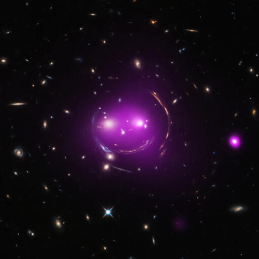 Albert Einstein's general theory of relativity, published over 100 years ago, predicted the phenomenon of gravitational lensing. And that's what gives these distant galaxies such a whimsical appearance, seen through the looking glass of X-ray and optical image data from the Chandra and Hubble space telescopes. Nicknamed the Cheshire Cat galaxy group, the group's two large elliptical galaxies are suggestively framed by arcs. The arcs are optical images of distant background galaxies lensed by the foreground group's total distribution of gravitational mass. Of course, that gravitational mass is dominated by dark matter. The two large elliptical "eye" galaxies represent the brightest members of their own galaxy groups which are merging. Their relative collisional speed of nearly 1,350 kilometers/second heats gas to millions of degrees producing the X-ray glow shown in purple hues. Curiouser about galaxy group mergers? The Cheshire Cat group grins in the constellation Ursa Major, some 4.6 billion light-years away. Image Credit: X-ray - NASA / CXC / J. Irwin et al. ; Optical - NASA/STScI.